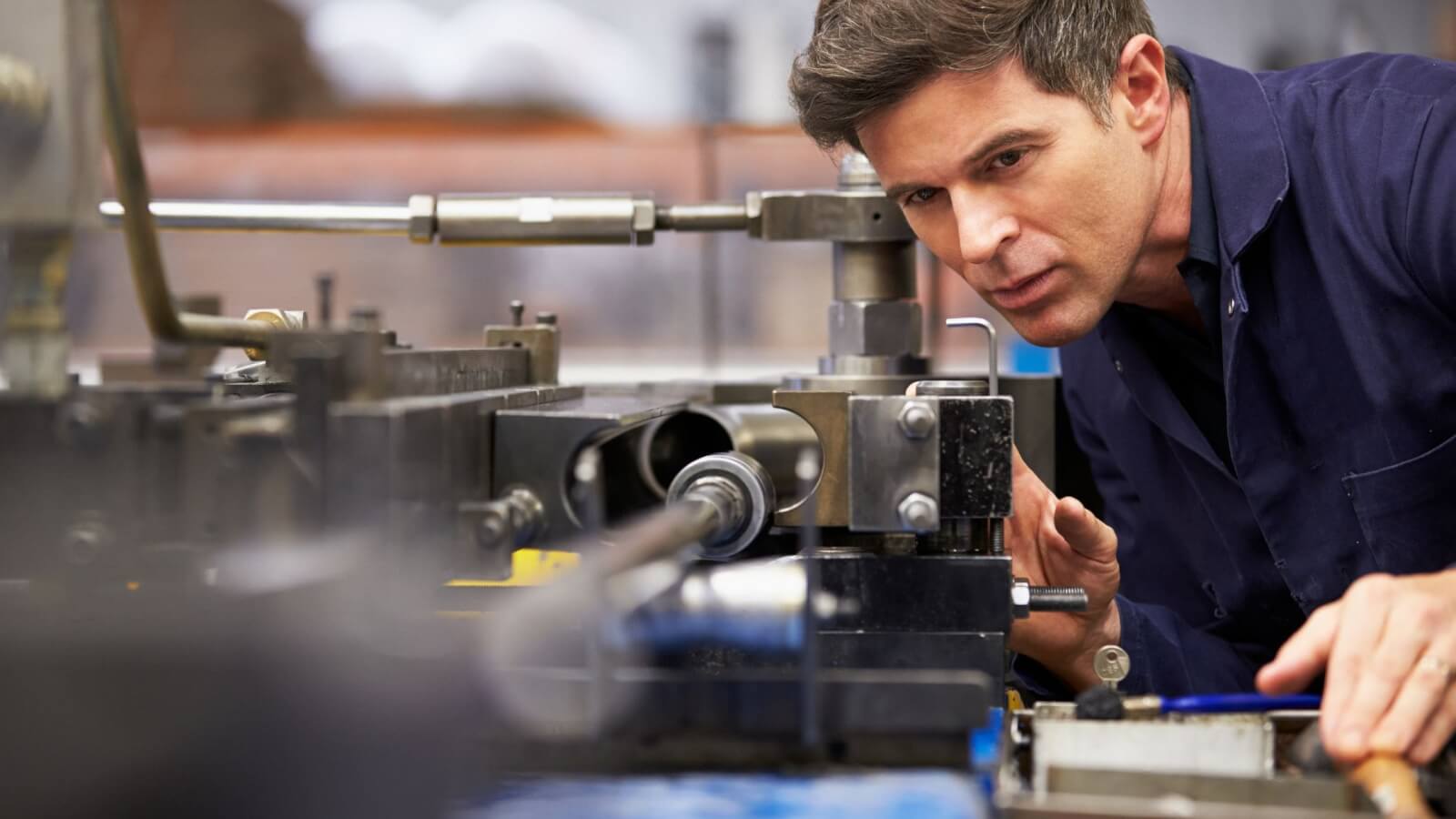 اپراتور دستگاه تراش CNC در حال اندازه‌گیری دقیق قطعه صنعتی تحت فشار کاری و نیاز به تمرکز بالا
